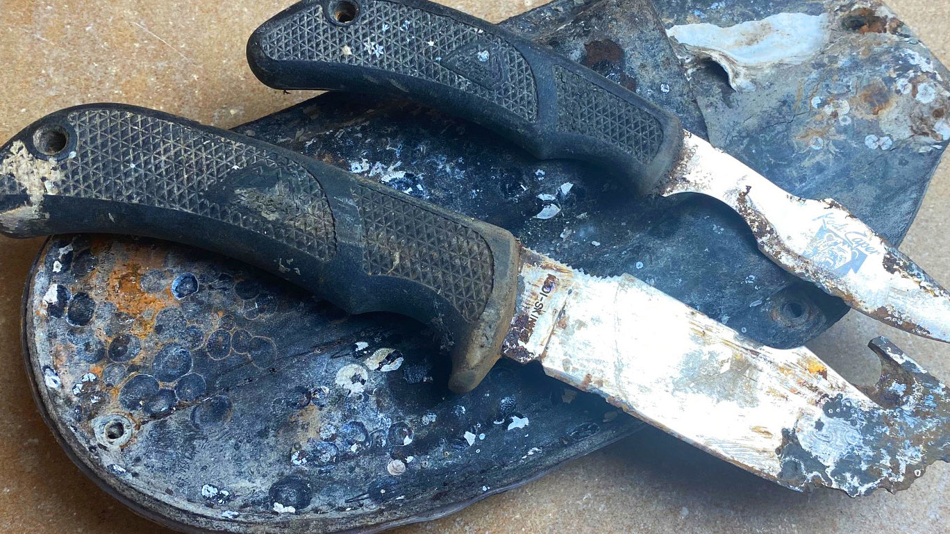 Two heavily corroded Outdoor Edge knives resting on a piece of debris after being recovered from saltwater four years after being lost in a hurricane