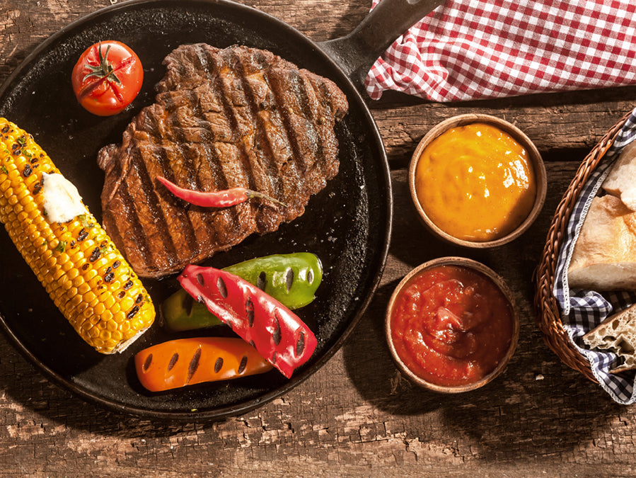 A wide, panoramic shot of a large bull elk grazing in a golden-yellow field, with a dense forest in the background showing hints of autumn color.