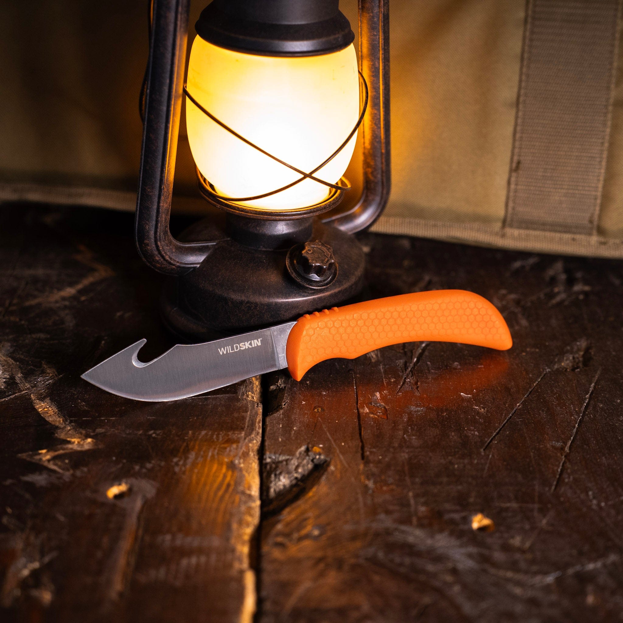 Knife with orange handle on a wooden surface next to a lantern