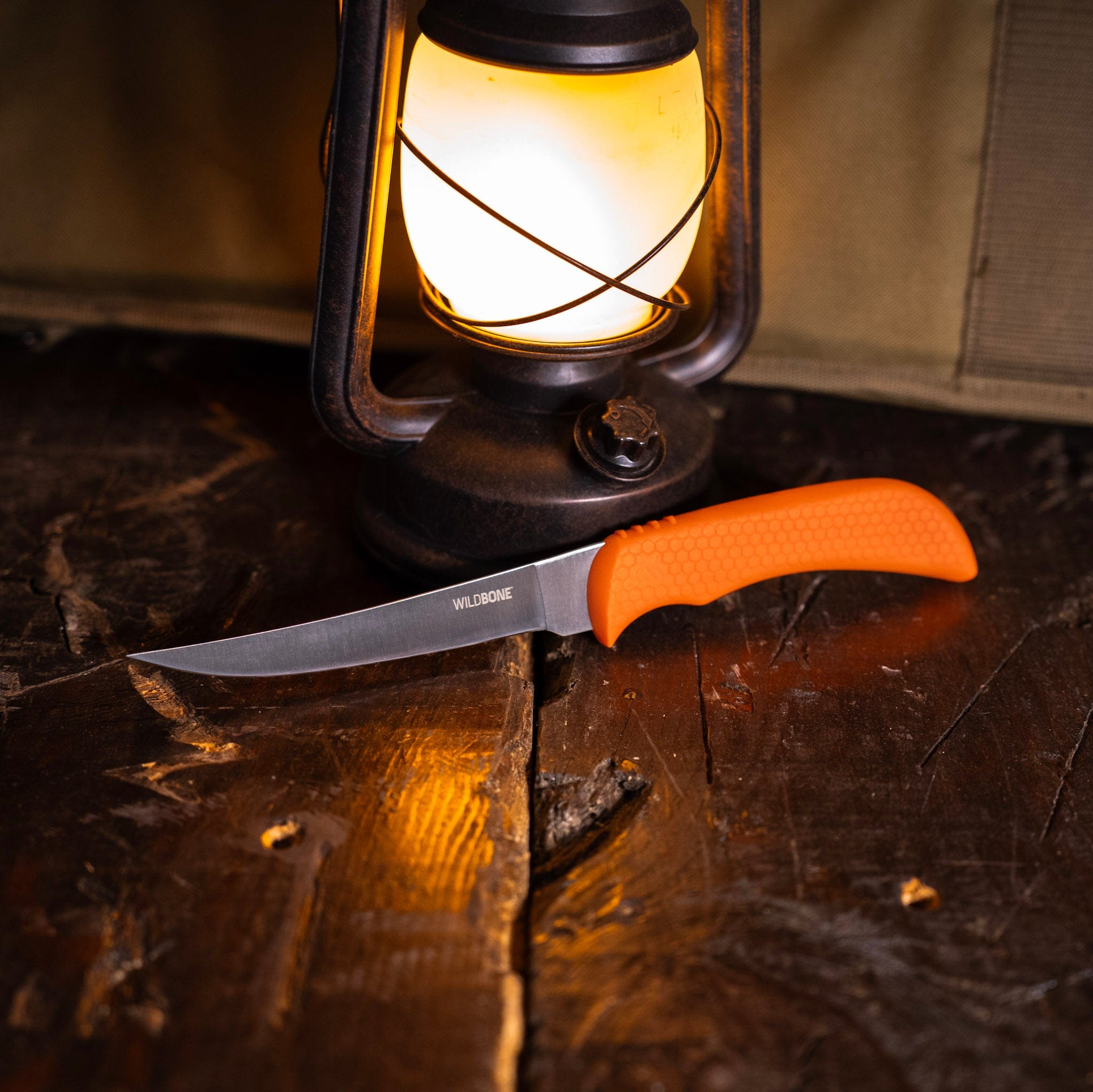 Knife with orange handle on a wooden surface next to a lantern