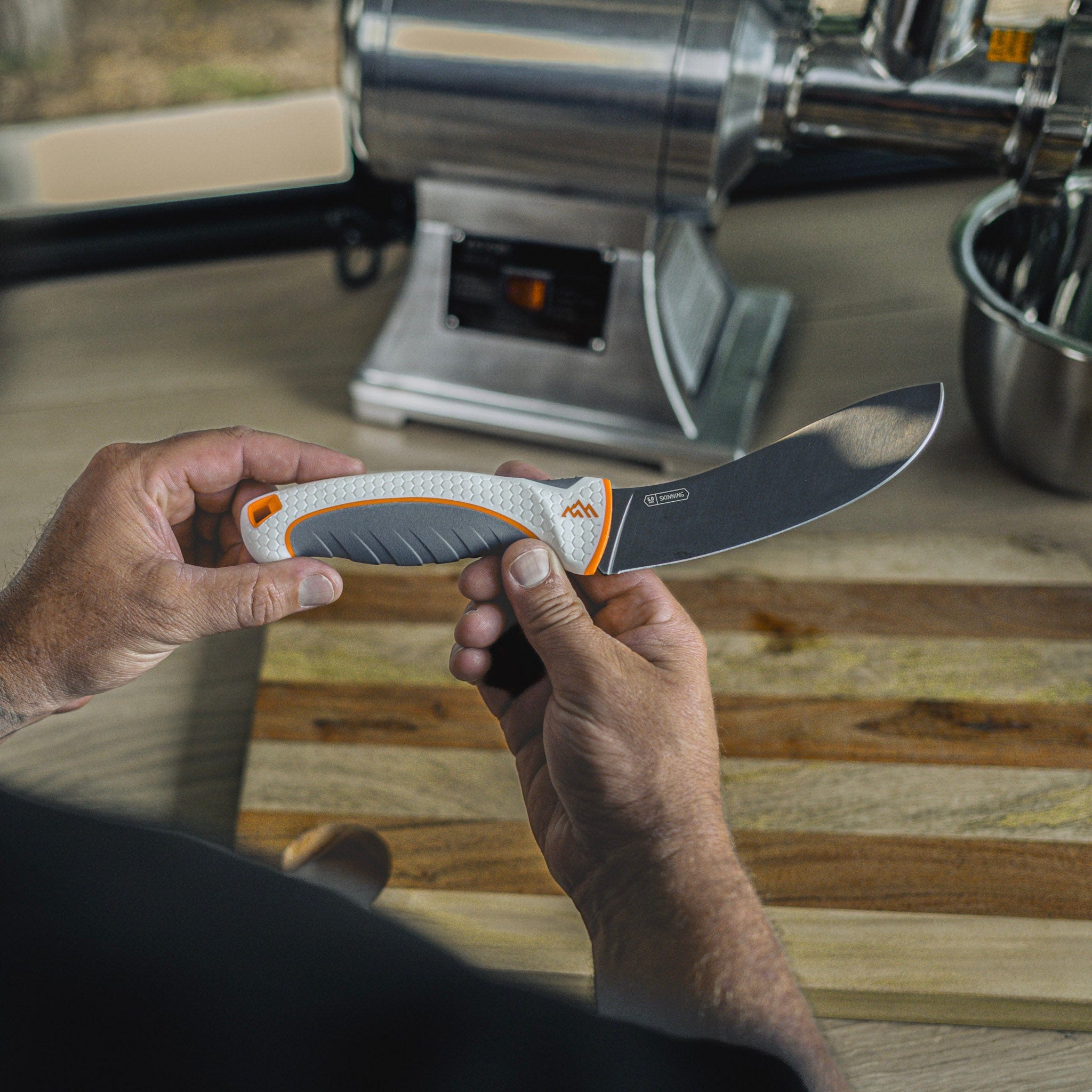 Person holding a knife with a wooden cutting board and kitchen appliance in the background