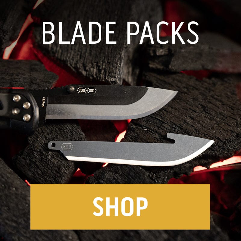 The Outdoor Edge RazorSafe system showing the handle with a drop-point blade and a separate gutting blade resting on hot coals."