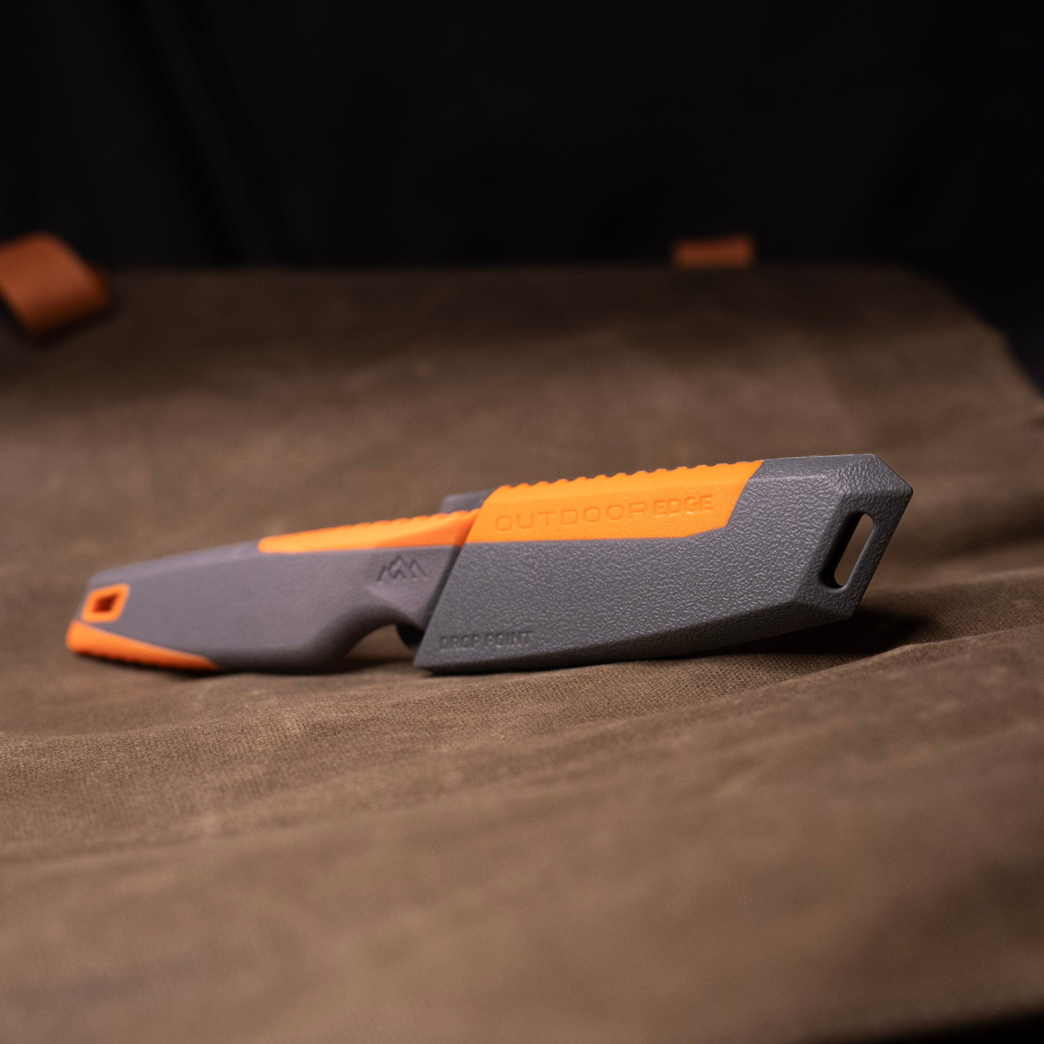 A knife with an orange and gray handle is lying on a brown fabric surface