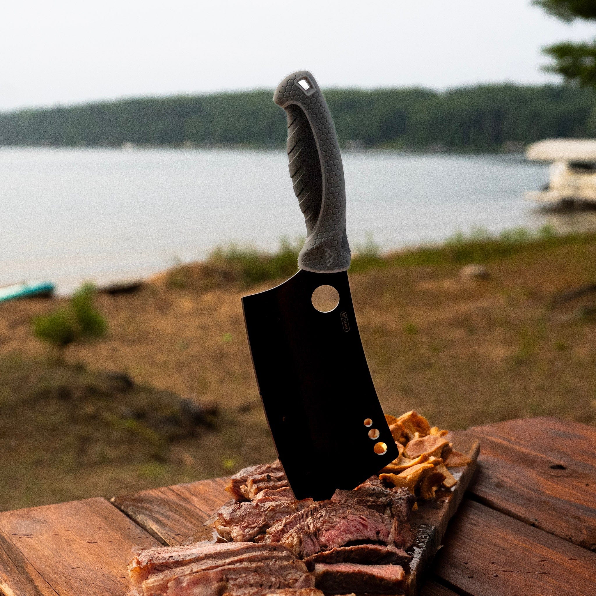 Meat cleaver on a wooden cutting board with a lake and boat in the background