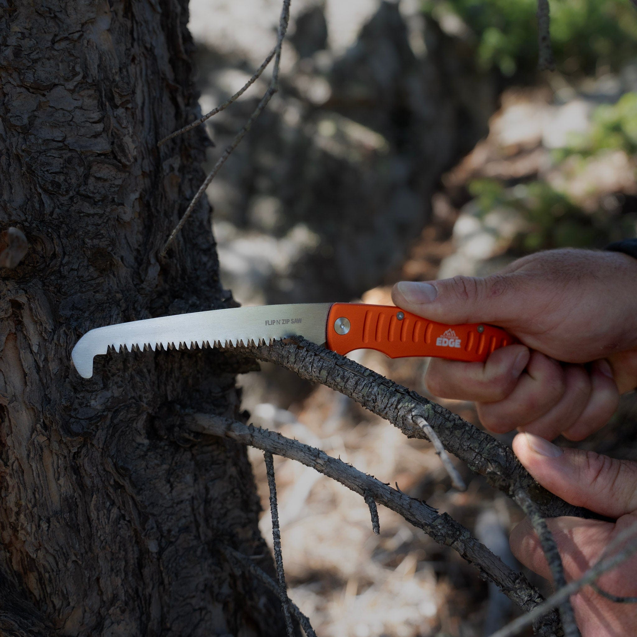 Hand holding a folding knife against a tree trunk in a natural setting