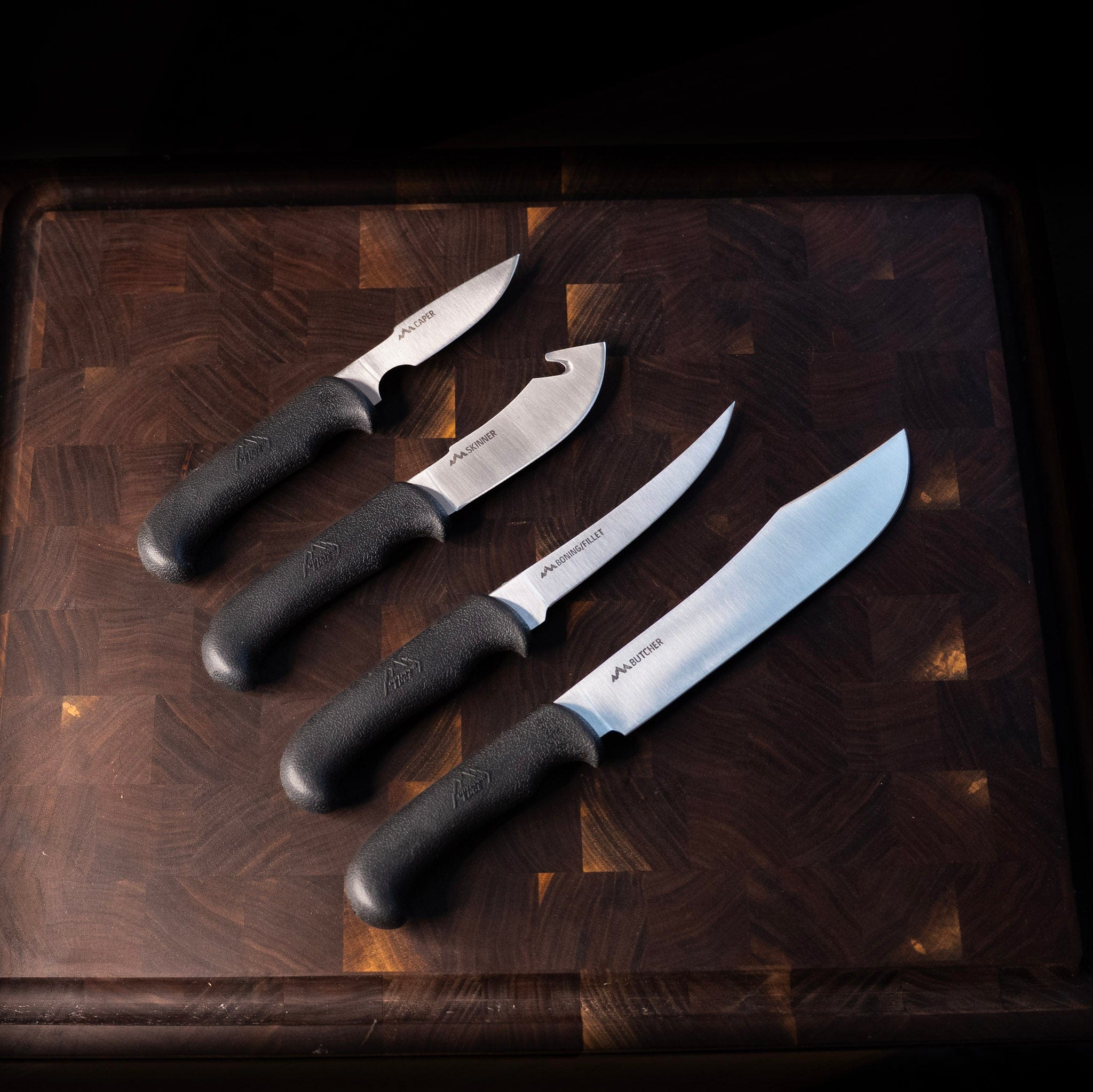 Four knives with black handles on a wooden cutting board