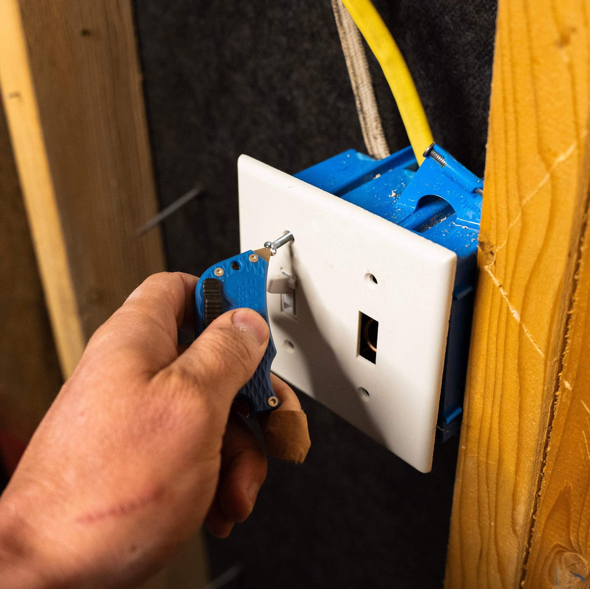 Hand using a blue tool to install or repair a white electrical outlet.