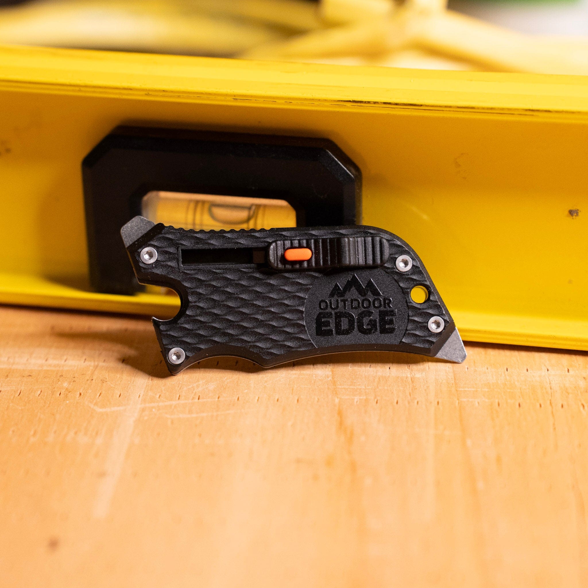 Small black utility knife sitting on a wood surface with tools in the background