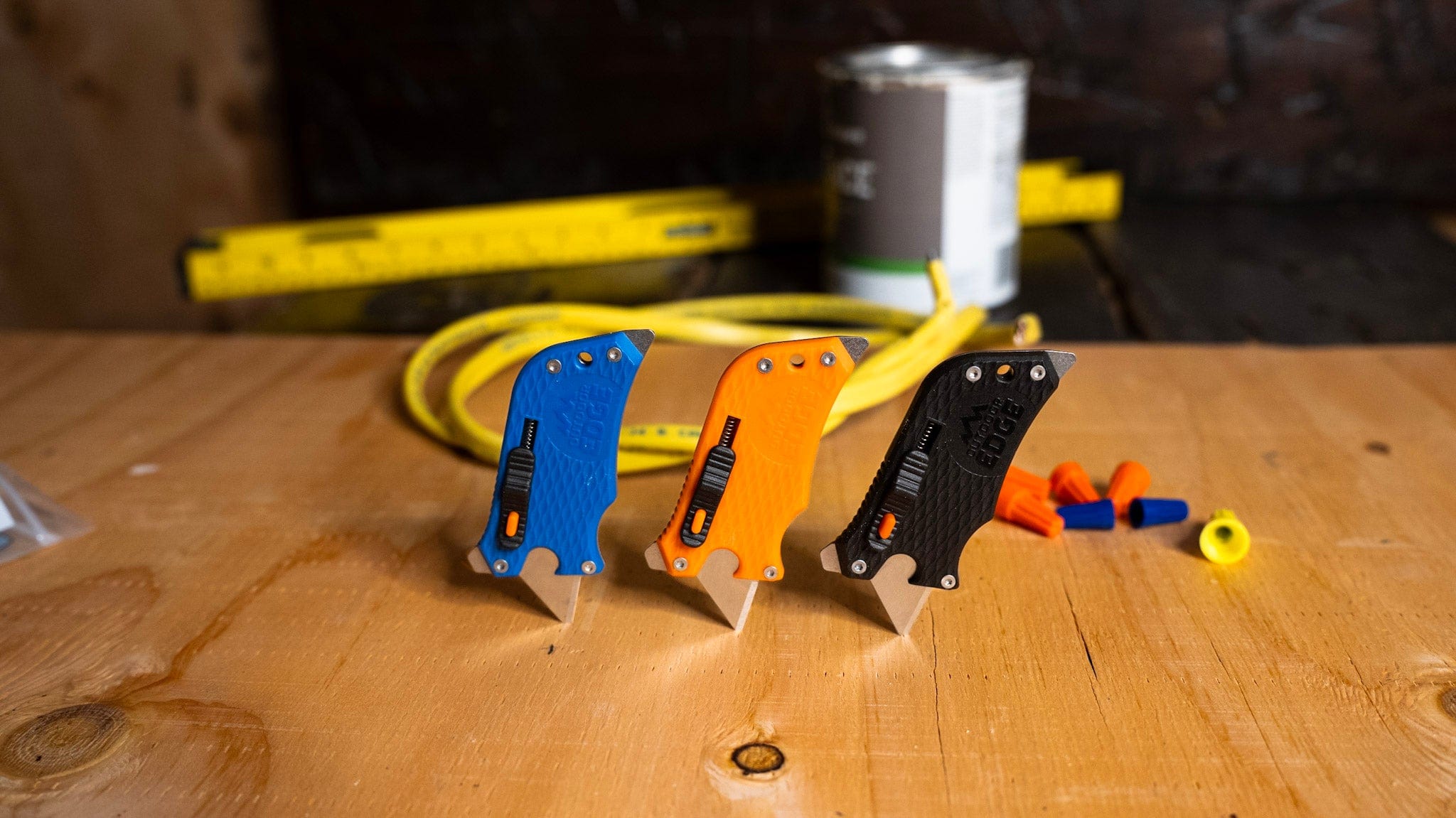Three colorful pocket knives on a wooden surface with tools in the background