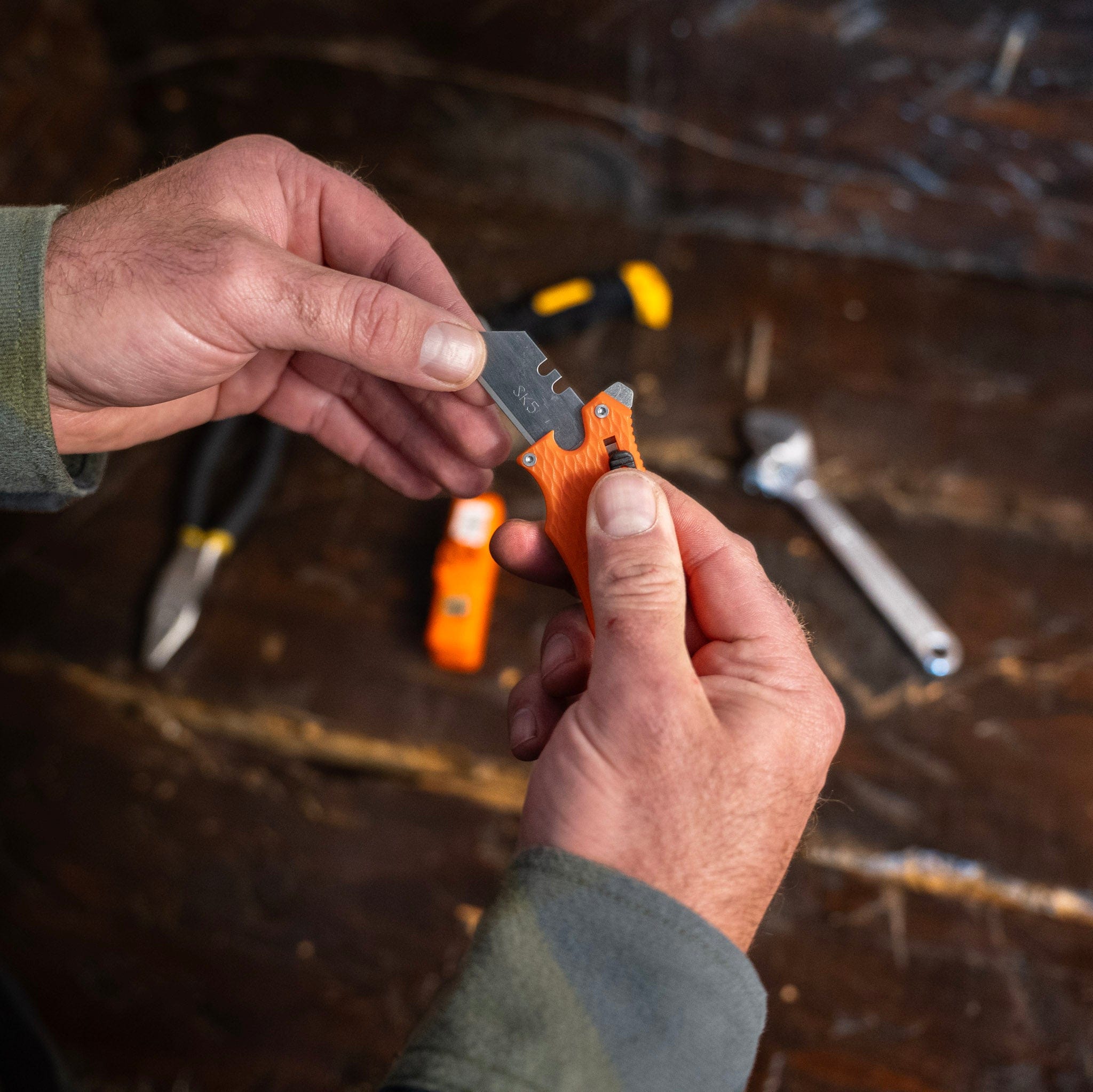A person changing a blade on a utility knife with tools in the background