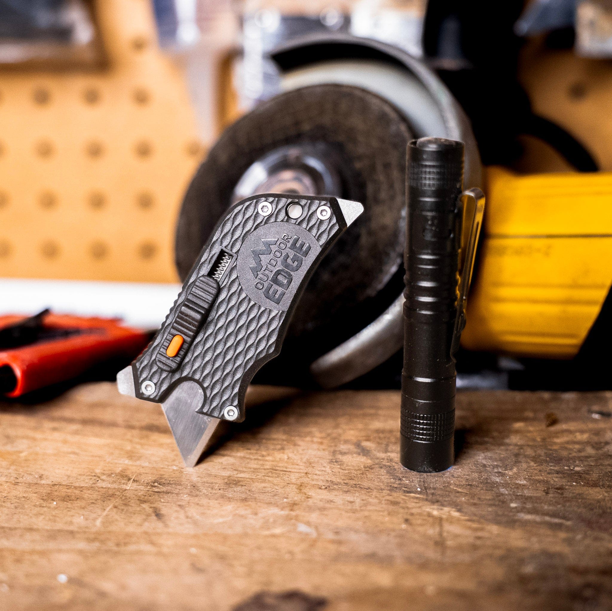 Knife and flashlight on a wooden surface with a power tool in the background