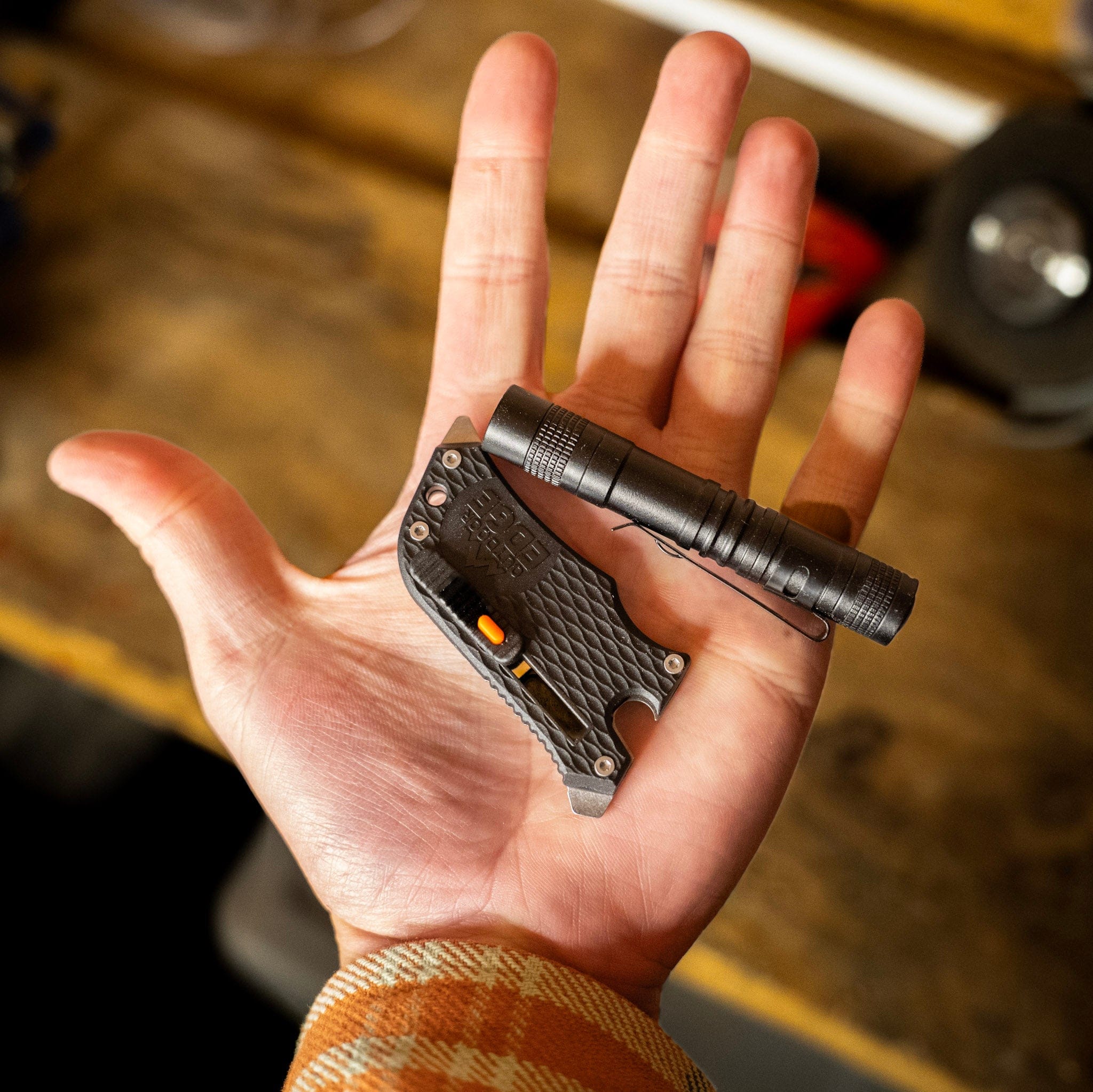 Hand holding a small black flashlight and utility knife on a blurred background