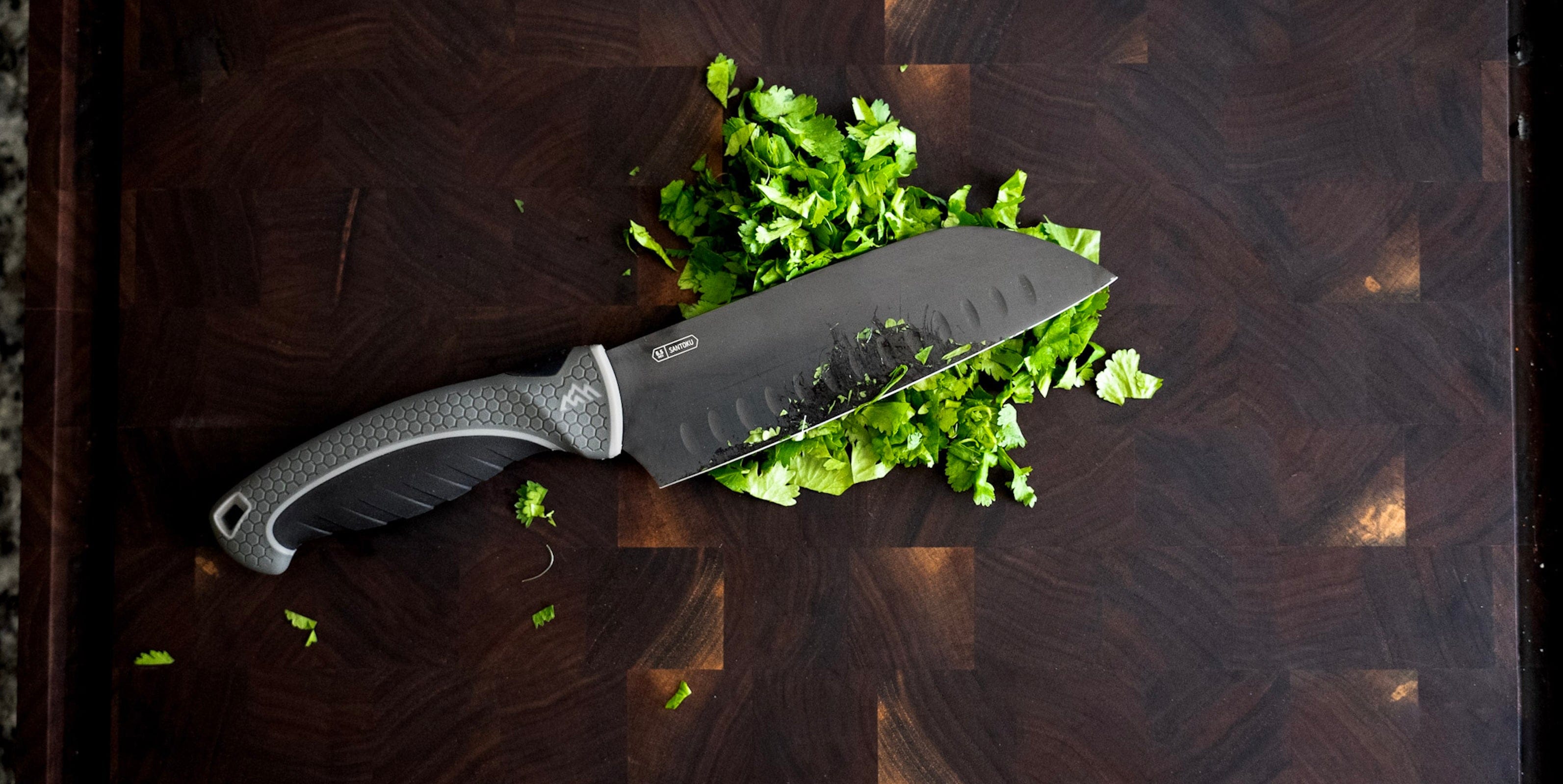 Chef's knife on a wooden cutting board with chopped green vegetables