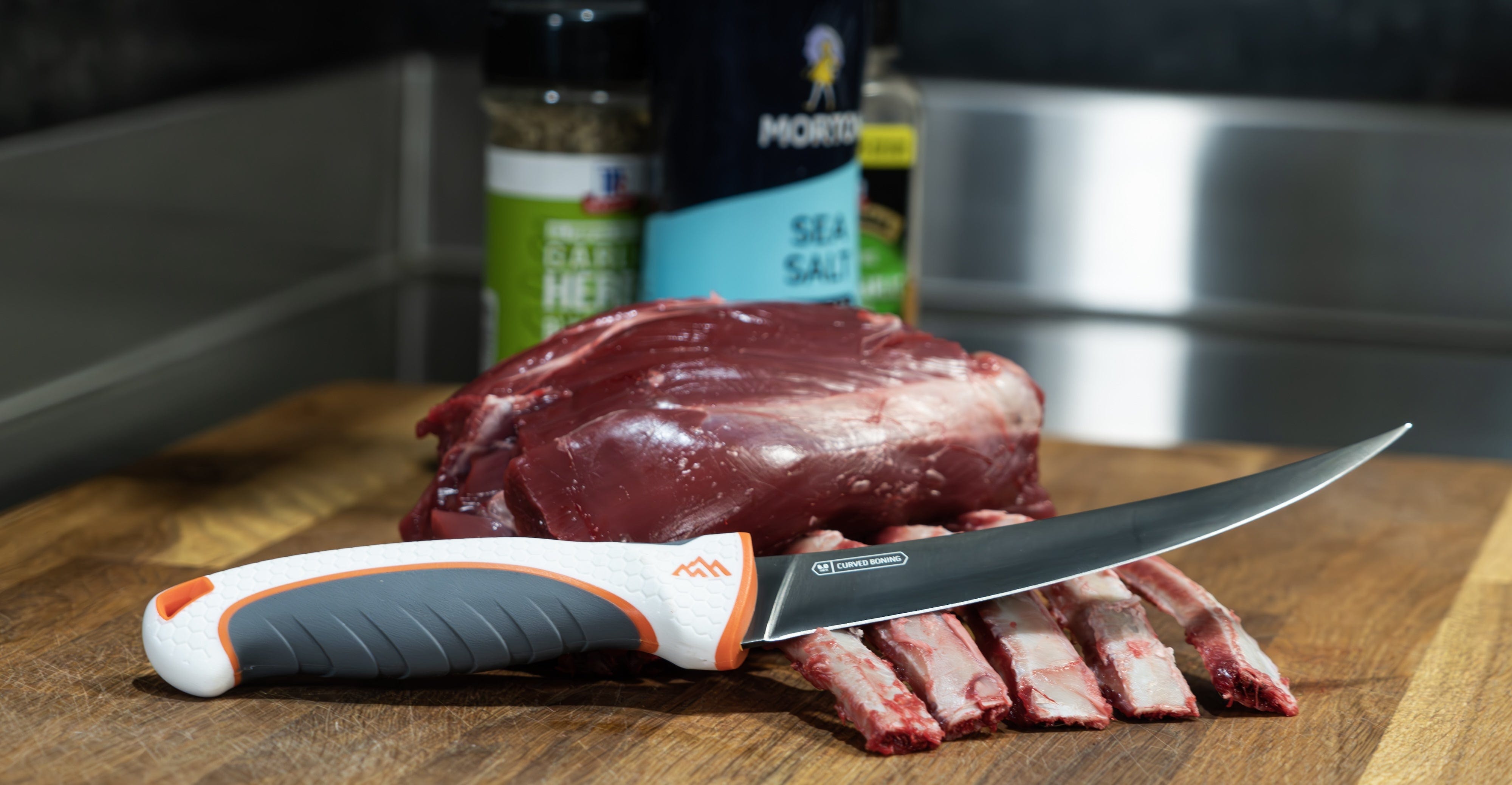 A variety of foods, including steak, salt, and spices, arranged with the ErgoMax knife