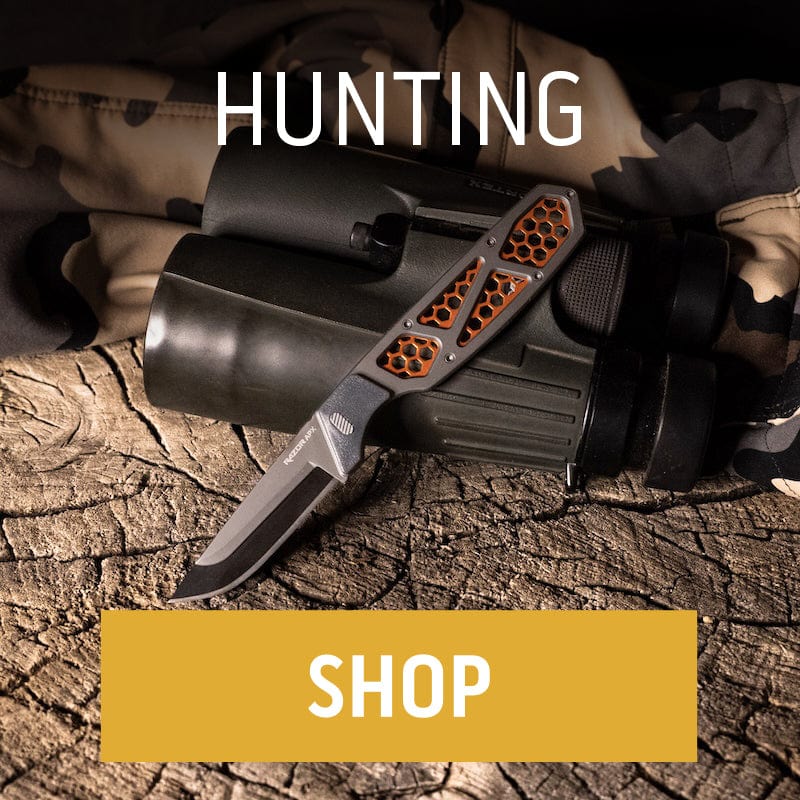 An Outdoor Edge hunting knife with a skeletonized orange and grey handle rests on a log next to binoculars and a camouflage jacket."