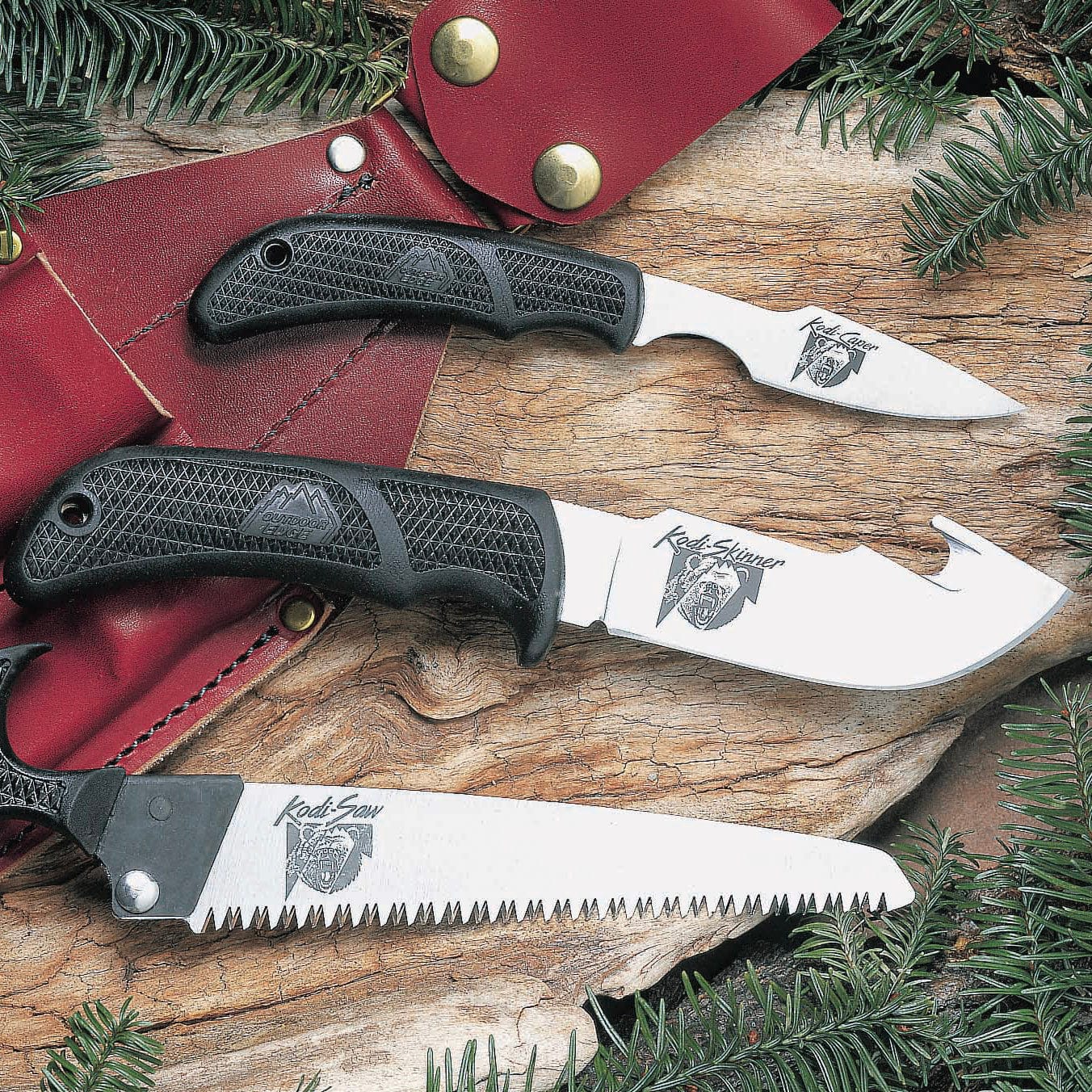 The original Outdoor Edge Game Skinner, Caper, and Saw combo with black handles displayed on a log with a leather sheath."