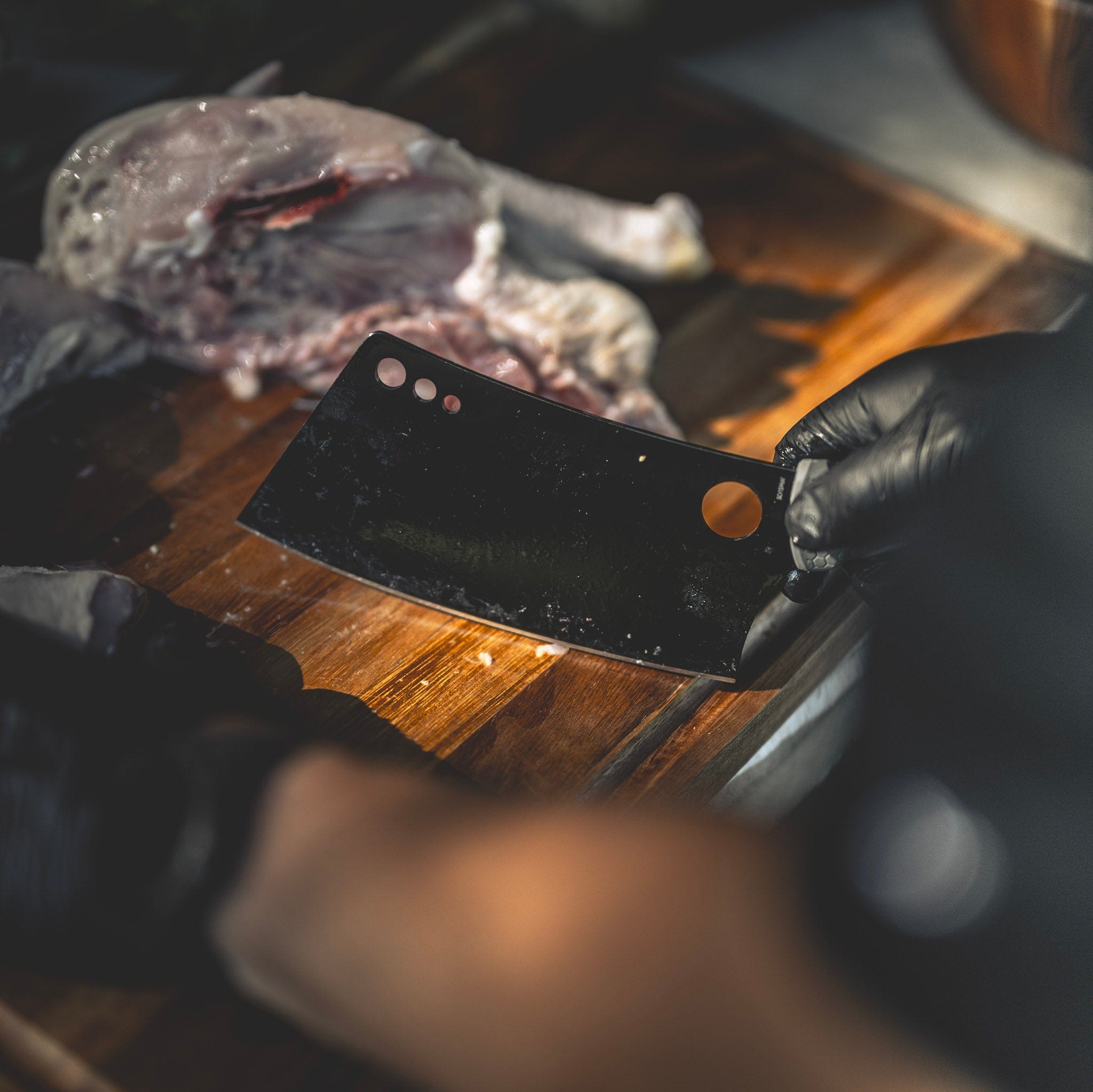 Cleaver knife breaking down raw chicken on a wooden cutting board