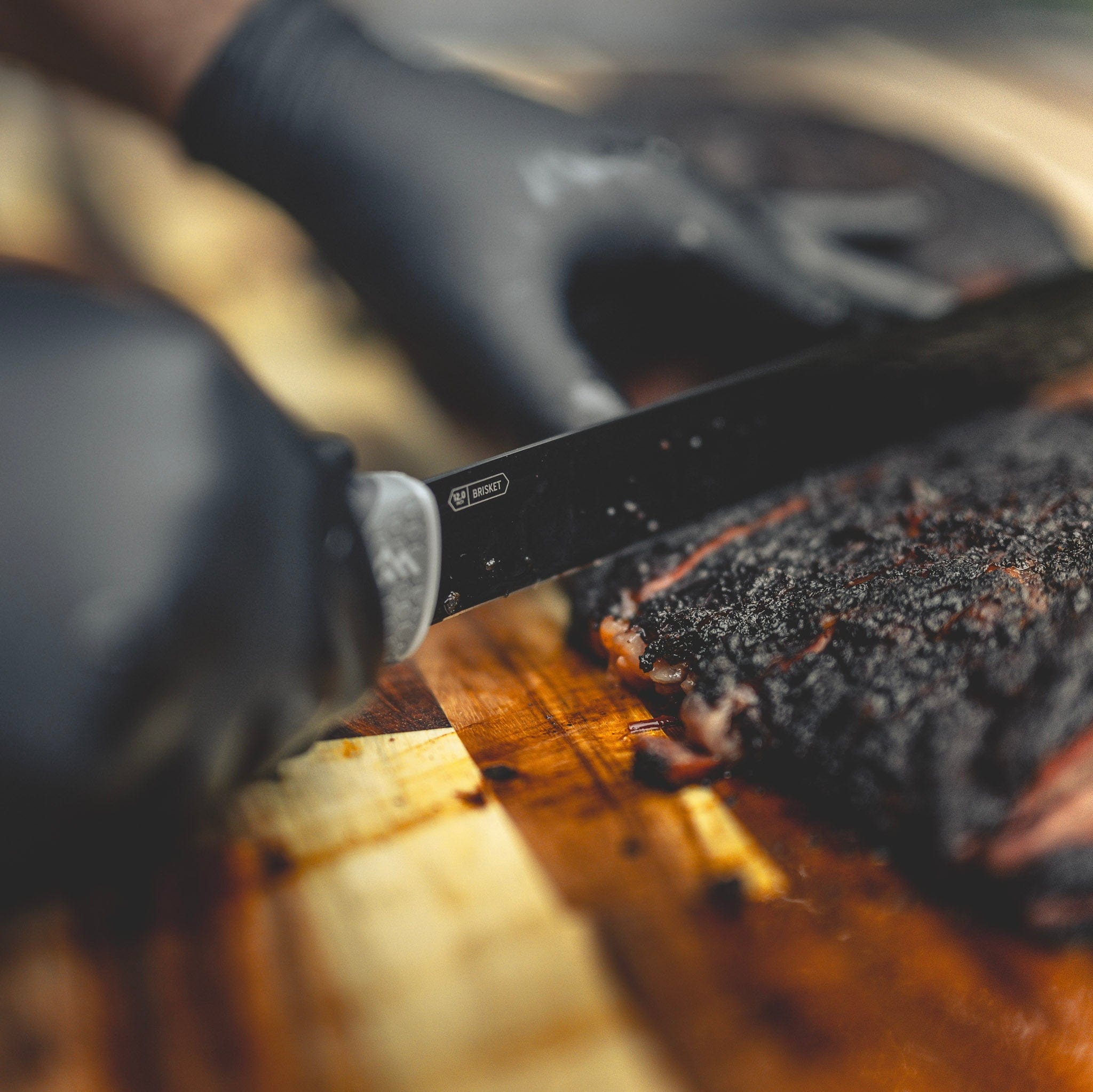 Person wearing black gloves slicing a brisket on wood cutting board