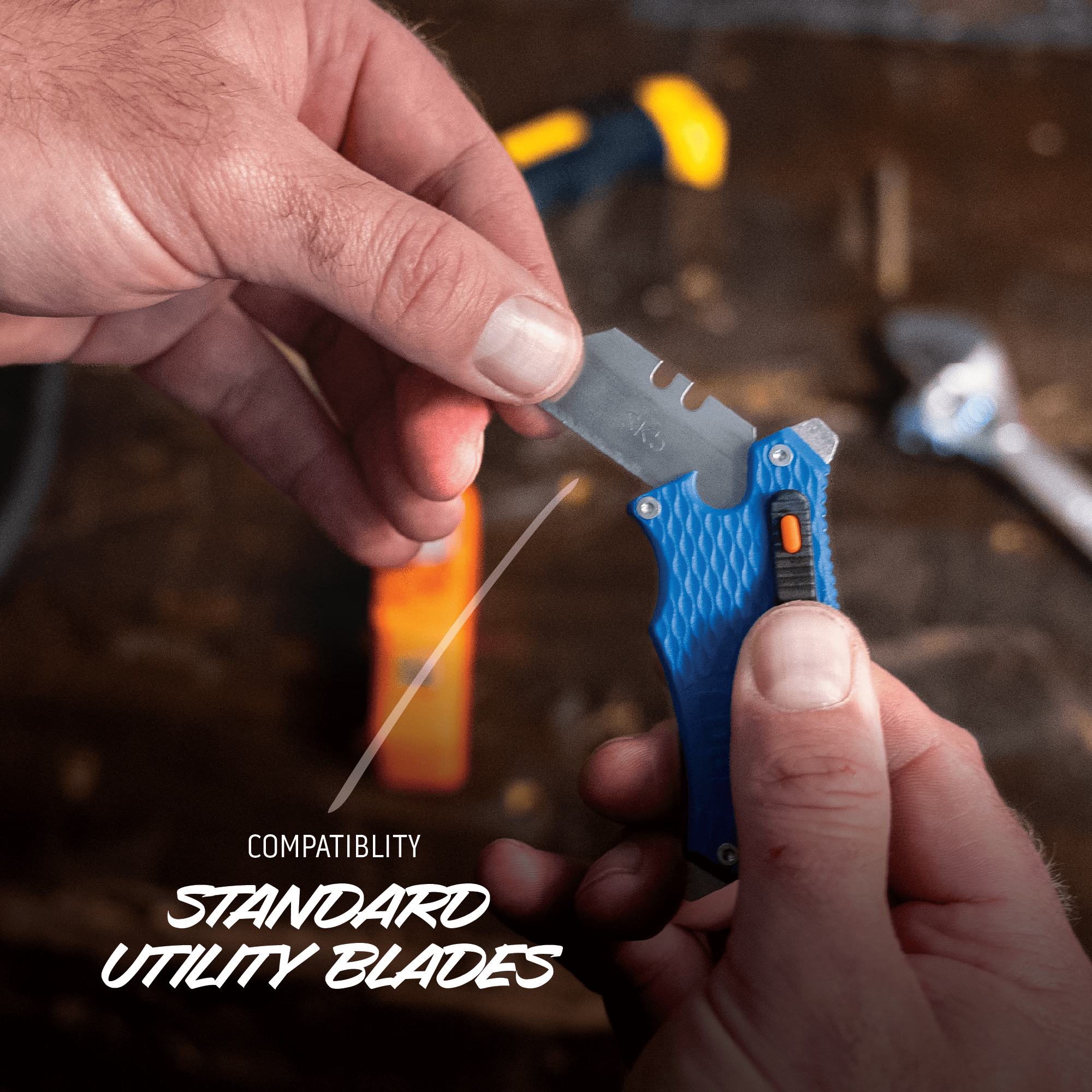 Person holding a small knife with a blue handle and a standard utility blade, with tools in the background.