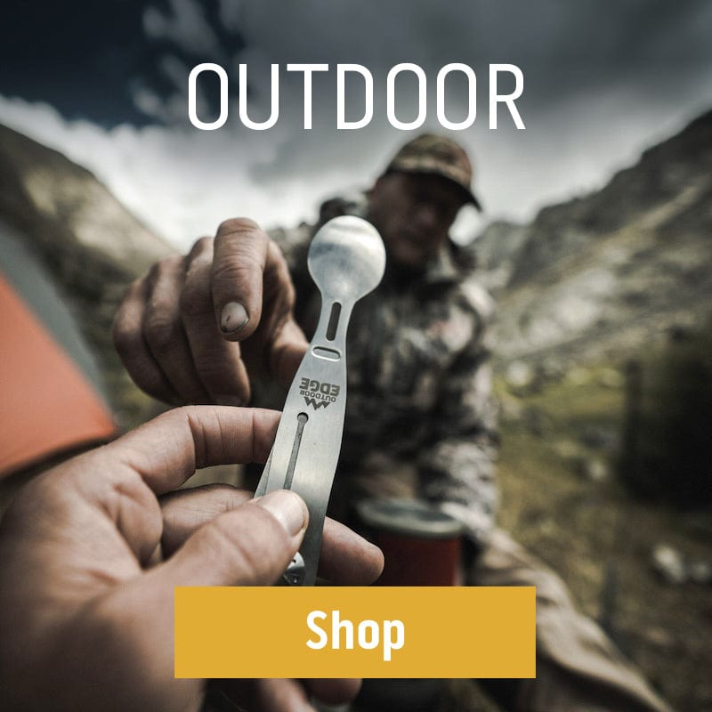 Camper holding an Outdoor Edge spork tool while sitting in a mountain campsite with a tent nearby.