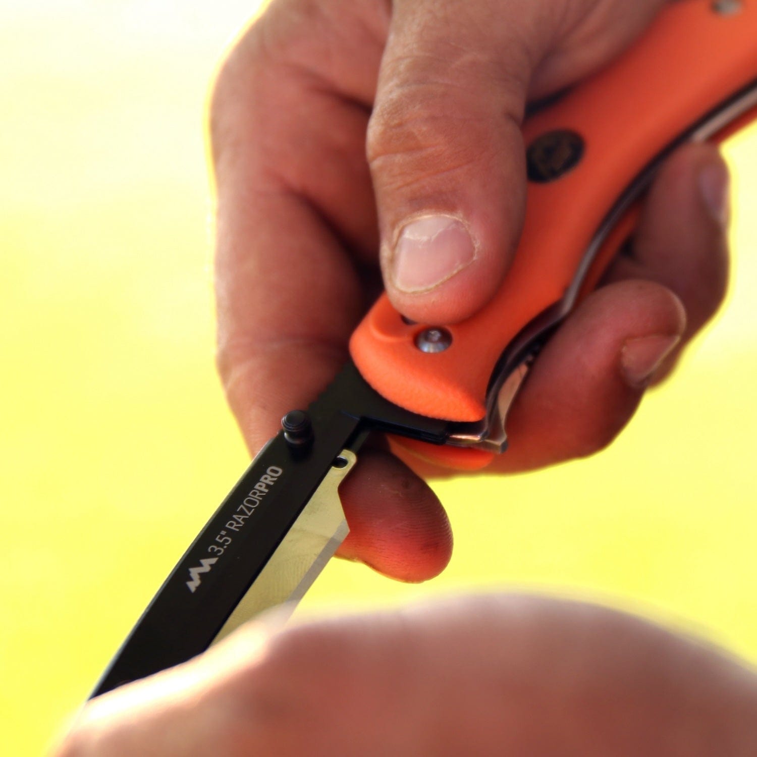"A close-up of a person's thumb pushing the blade of an orange-handled 3.5-inch RazorPro knife open. ",