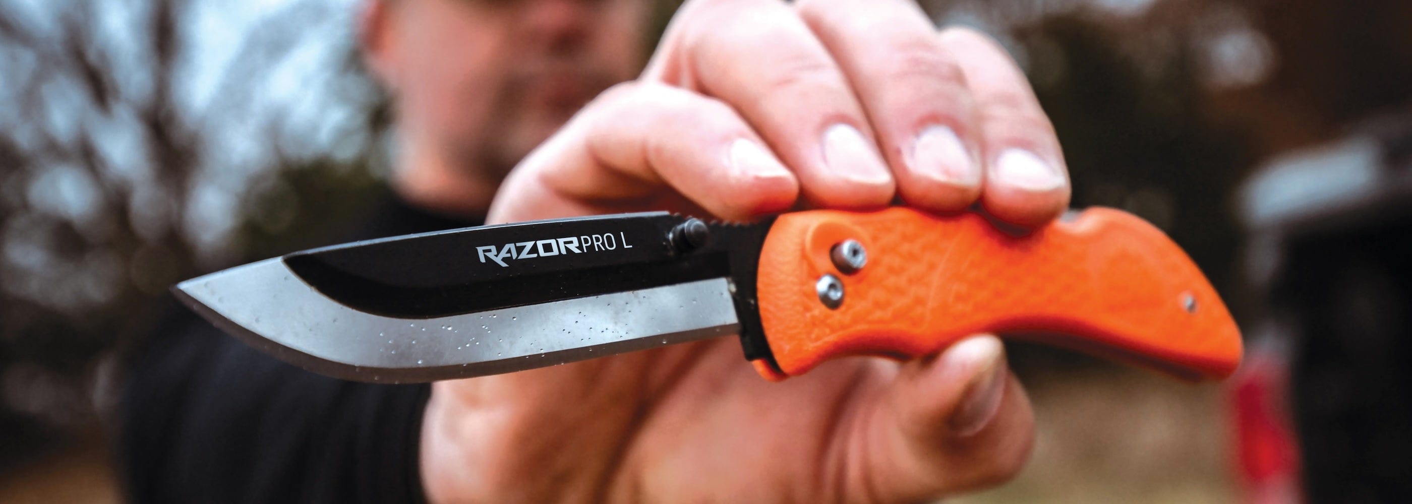"A person holding an open, orange-handled RazorPro-L knife."