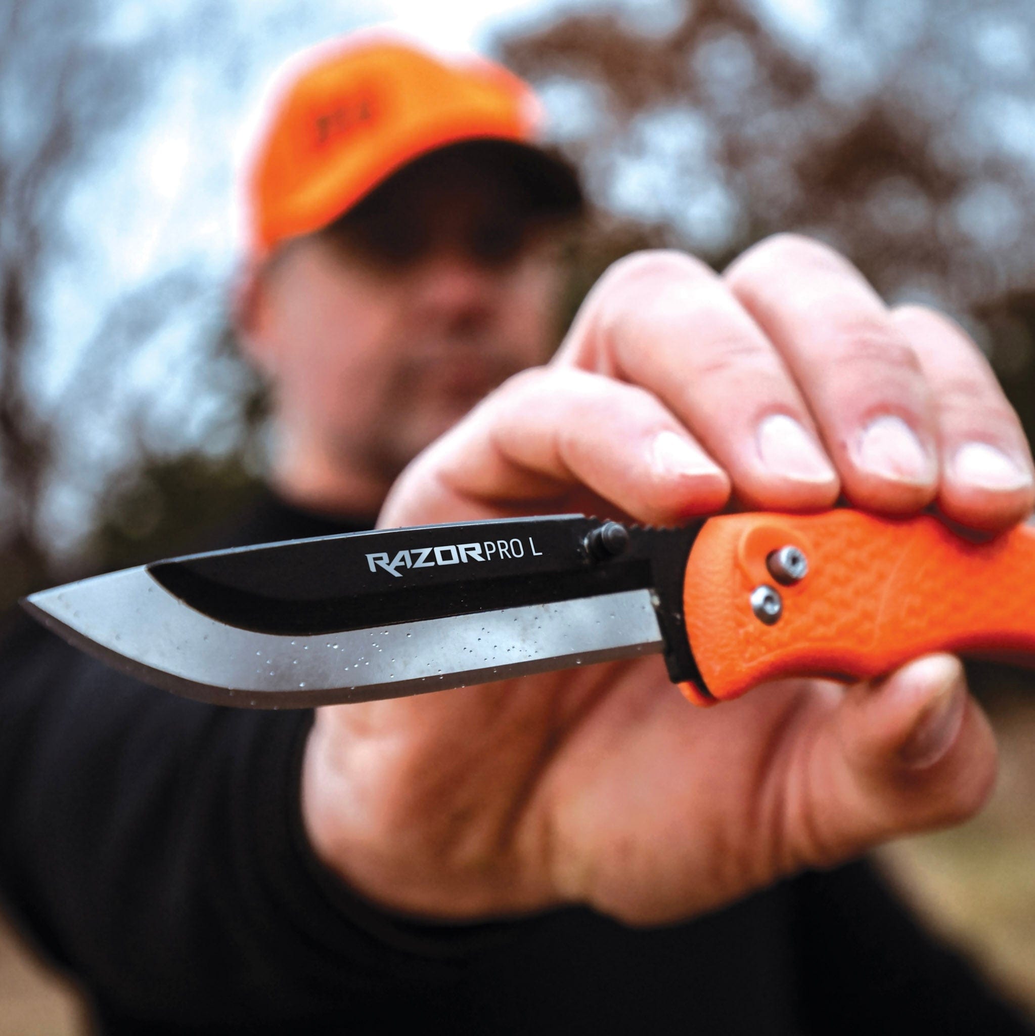"A close-up of a person holding an orange-handled Outdoor Edge RazorPro folding knife. "