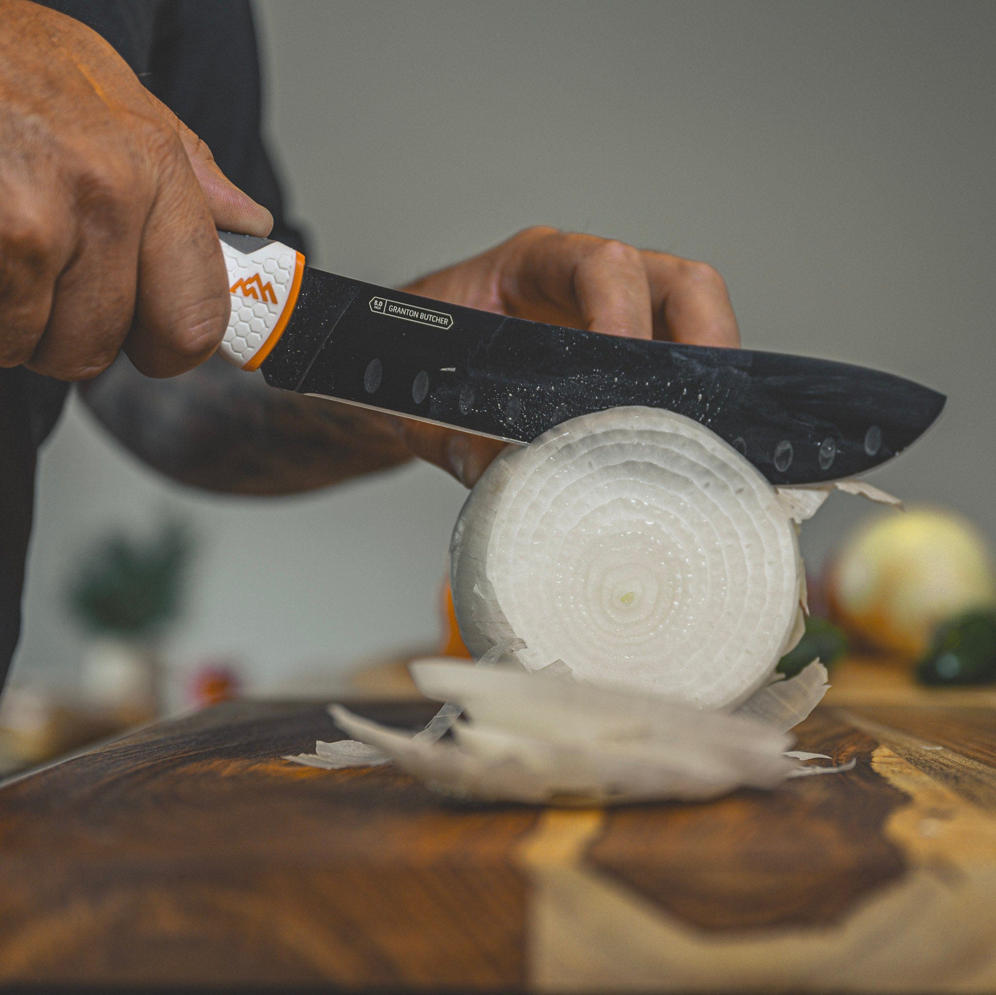 Person cutting an onion with a knife on a wooden cutting board