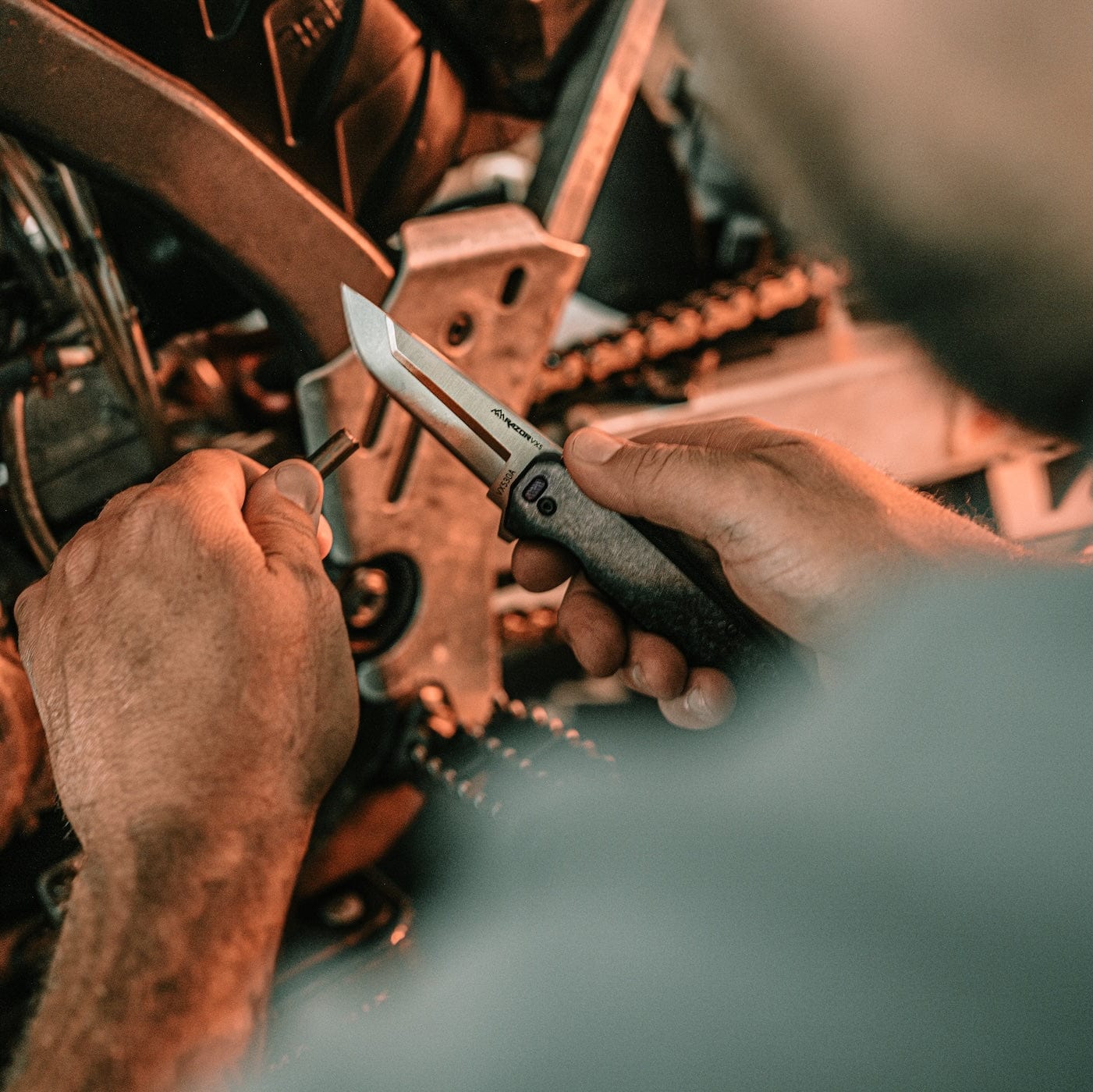 "An Outdoor Edge folding knife with a silver blade and black handle on a red workbench cluttered with nuts, bolts, and tools."
