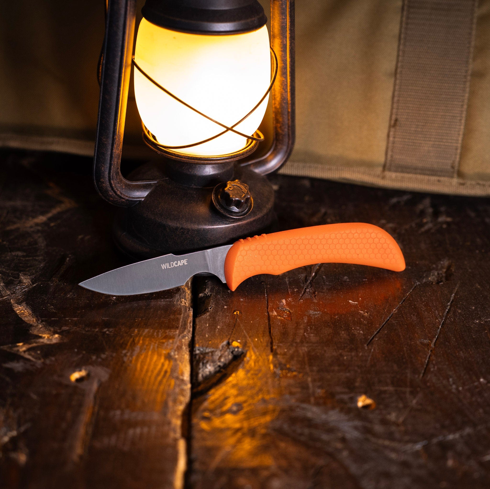 Knife with orange handle on a wooden surface next to a lit lantern