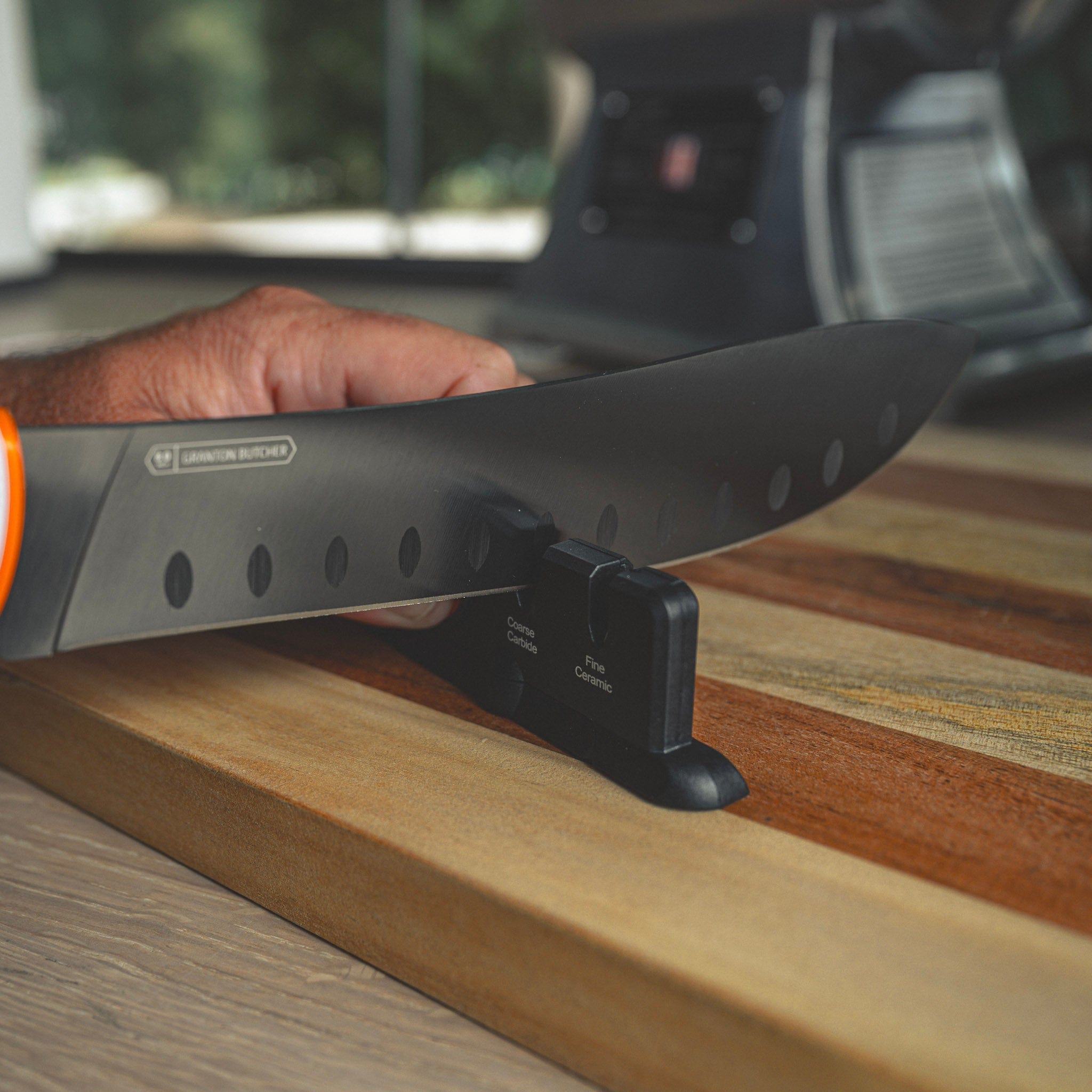 Person holding a large knife with a visible brand logo on a wooden surface.