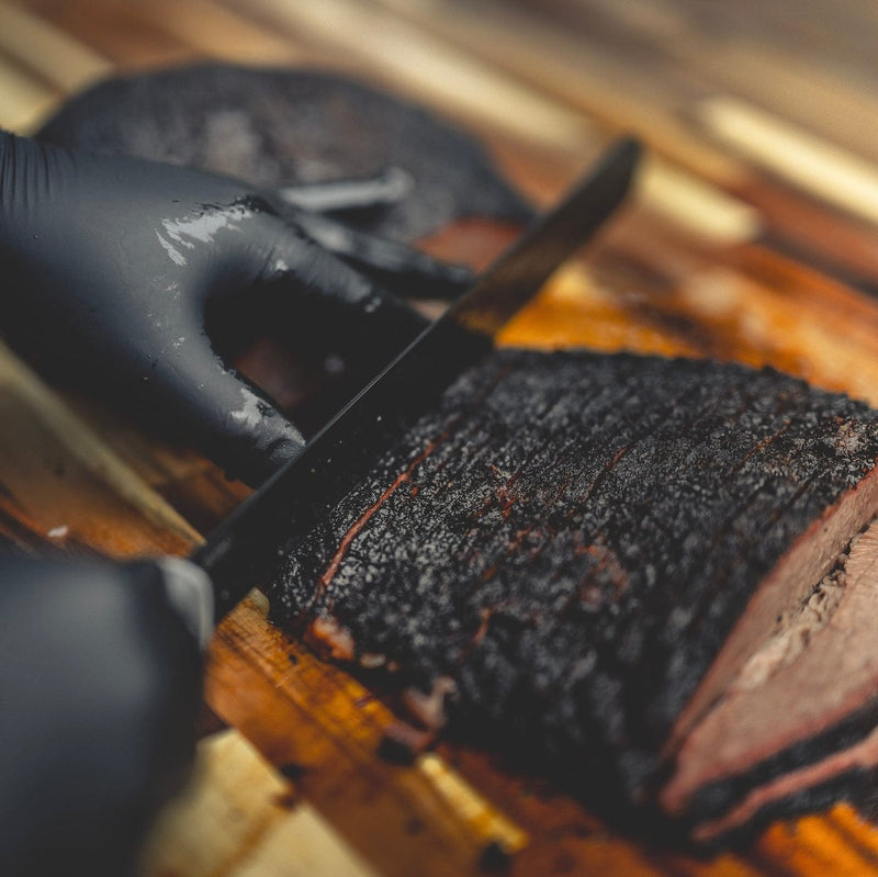 Person wearing black gloves cutting a roasted item on a wooden surface