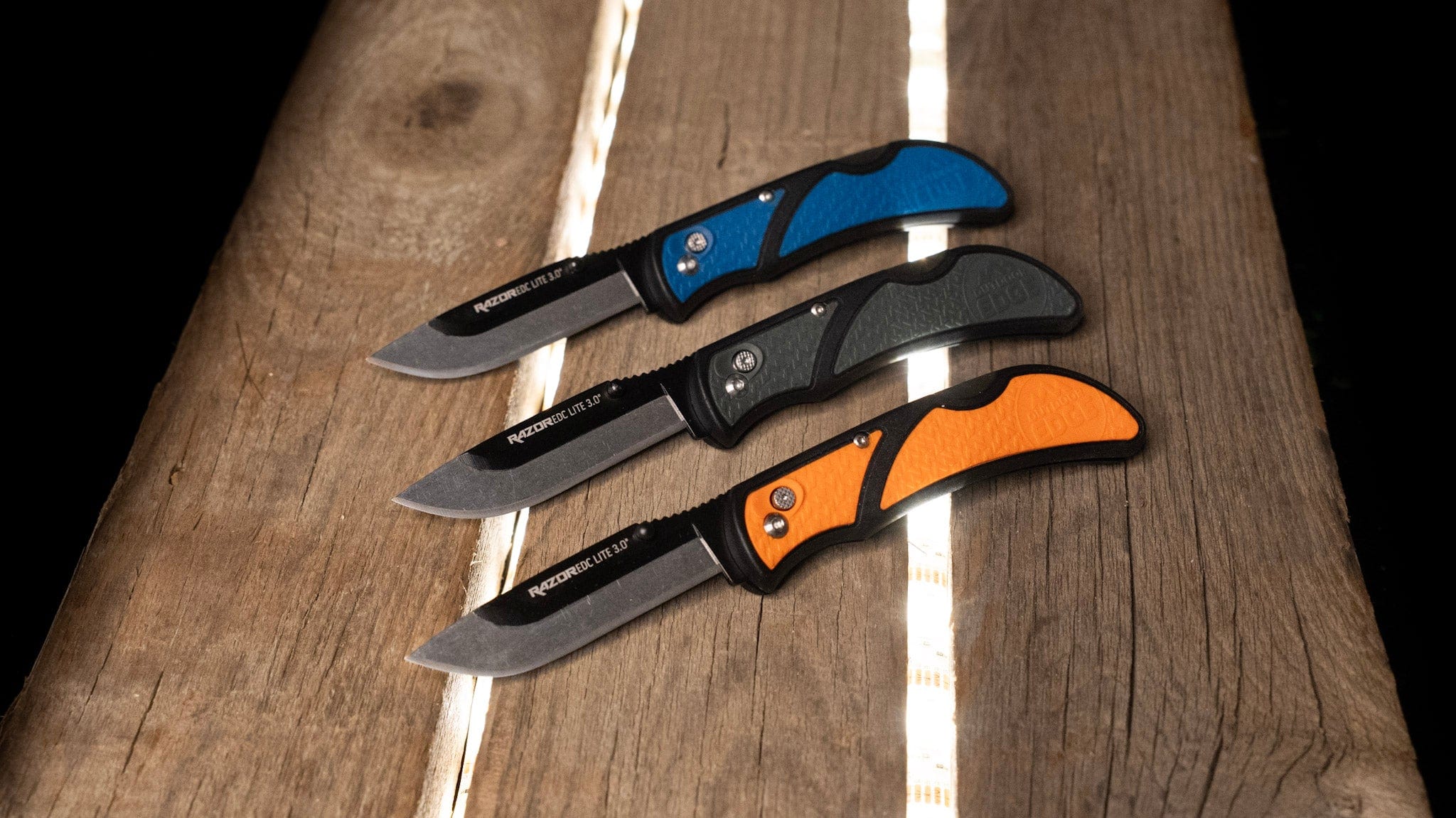 Blue, Orange and Grey knives sitting on backlit wood