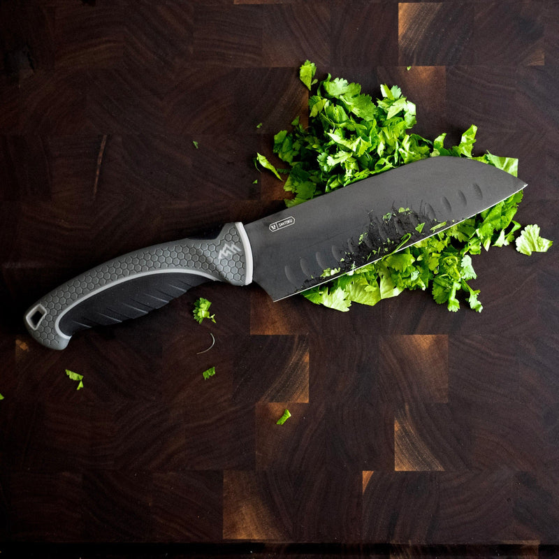Knife with a black blade and gray handle on a wooden surface with chopped green vegetables.