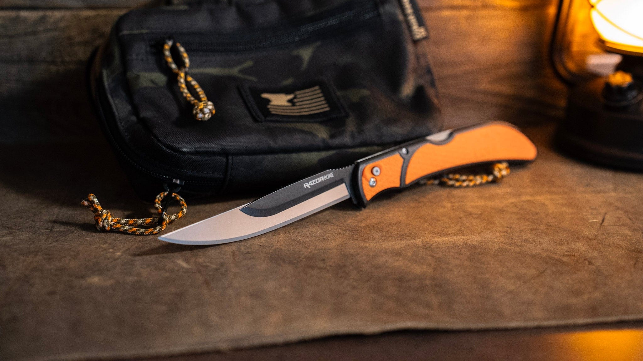 Knife with orange handle on a wooden surface next to a black bag.
