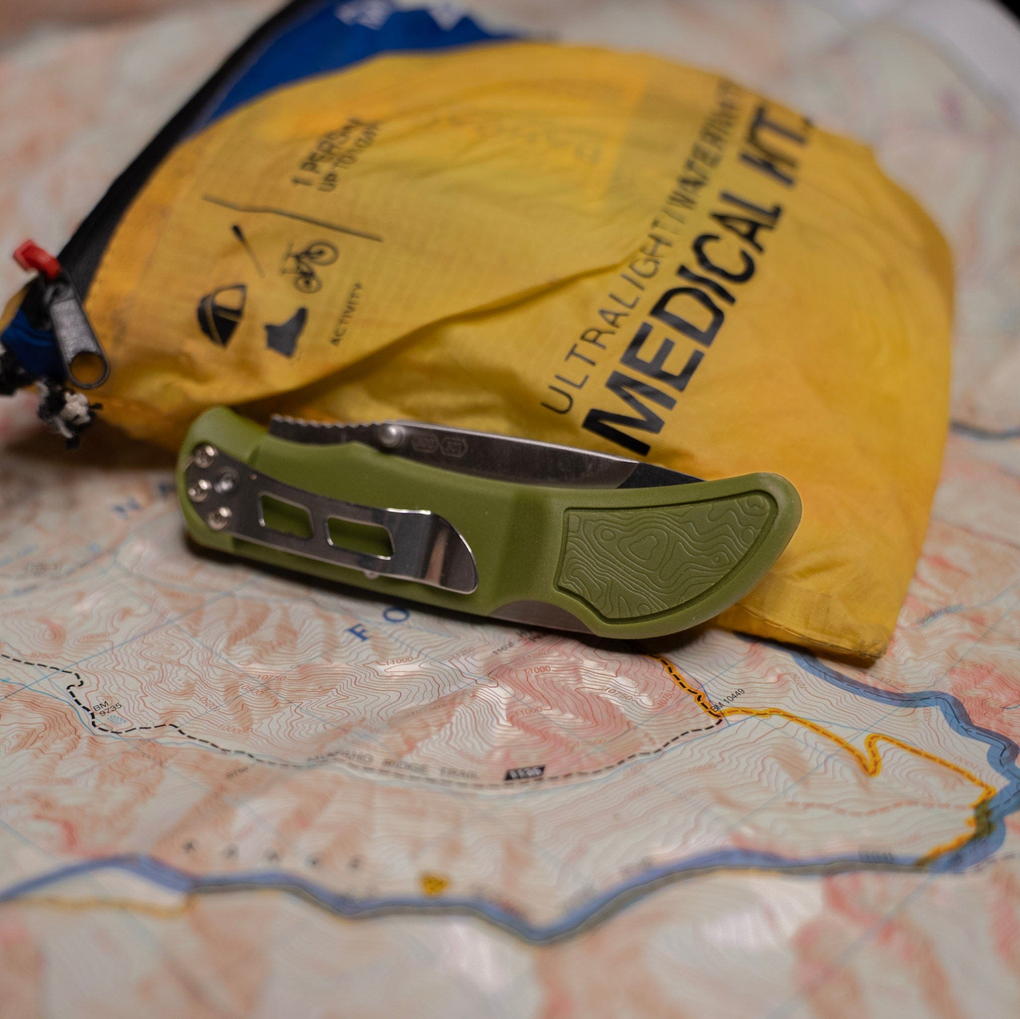 Green pocket knife on a map with a yellow medical kit in the background