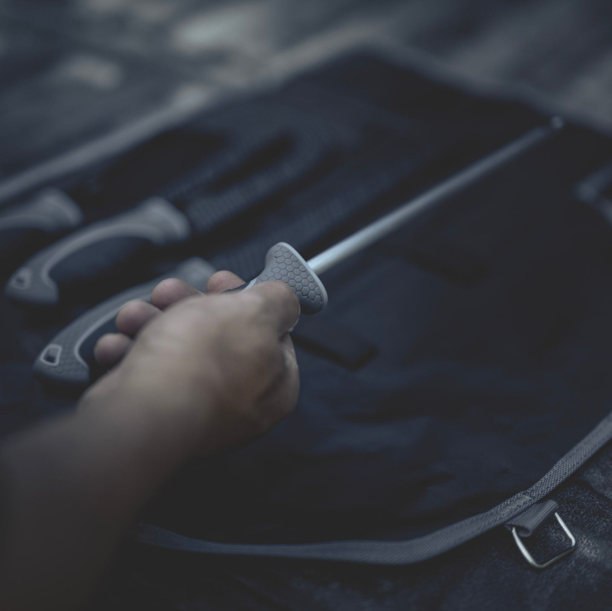 Hand holding a honing rod over an open roll pack with other knives inside.