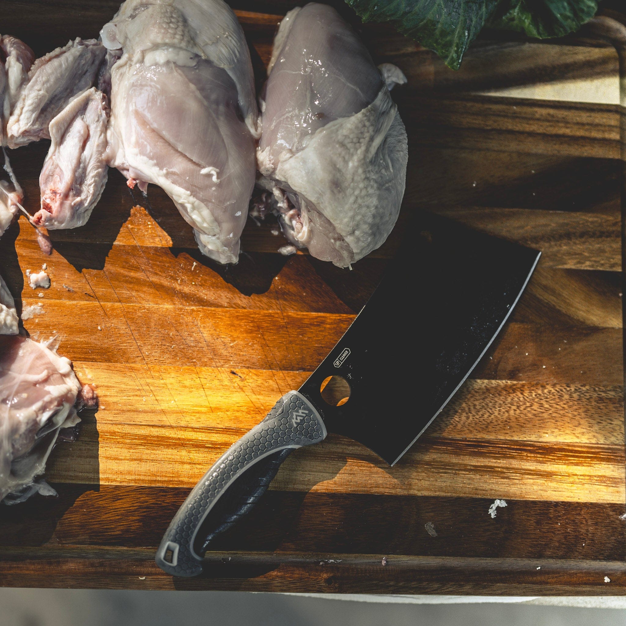 Raw chicken pieces on a wooden cutting board with a cleaver knife.