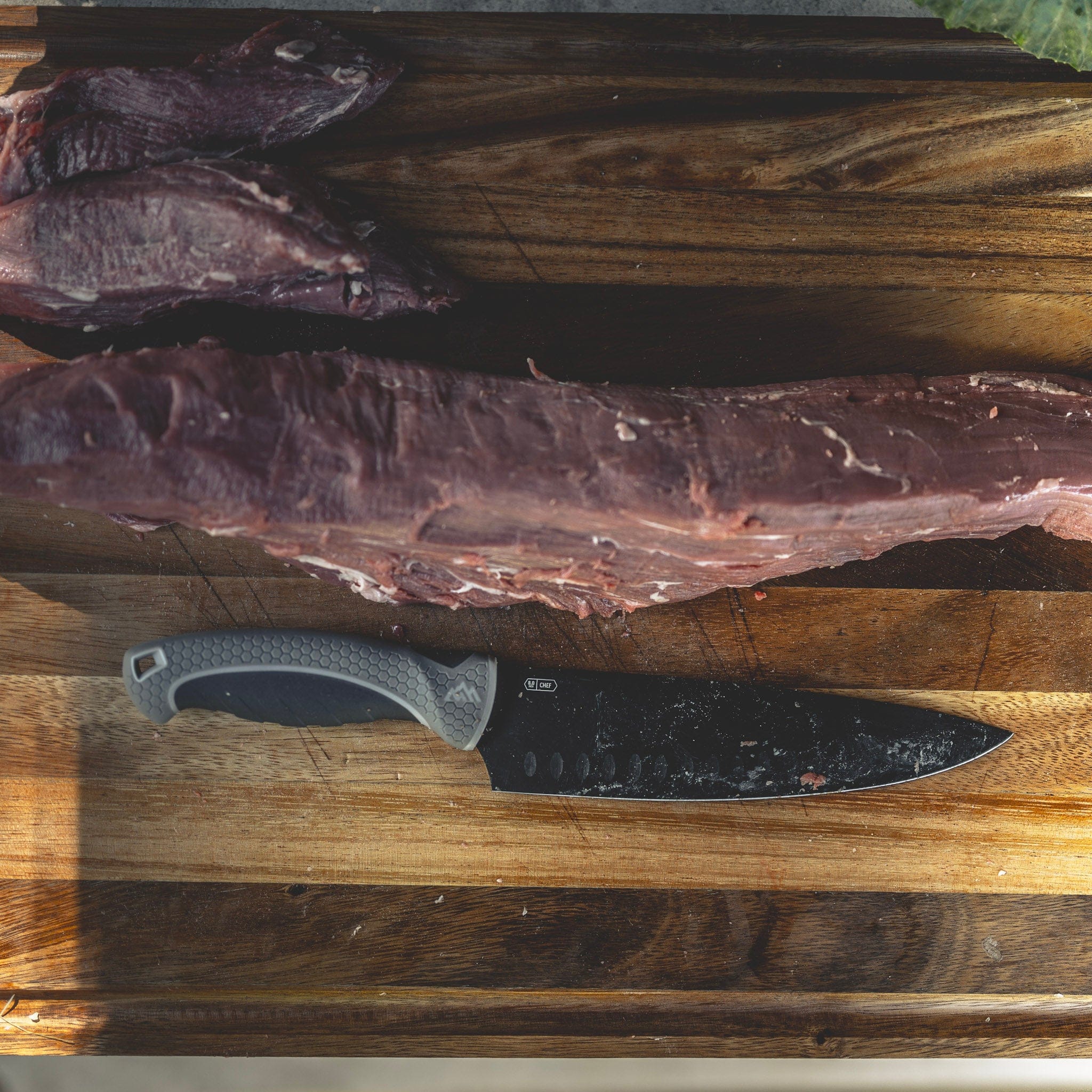 Knife on a wooden cutting board with cured meat