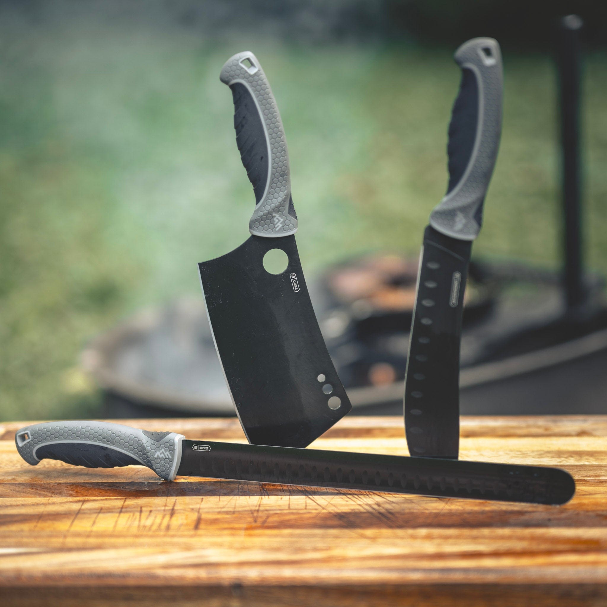 Three black knives with textured handles on a wooden surface, blurred natural background
