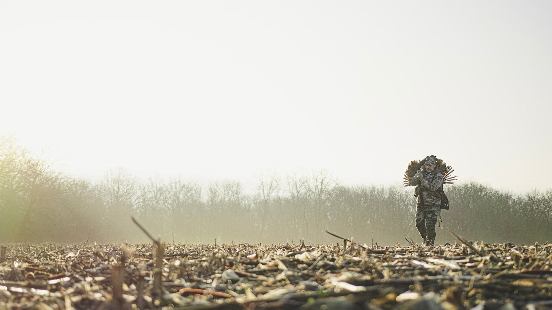 Person in camouflage walking through a field with a blurred background